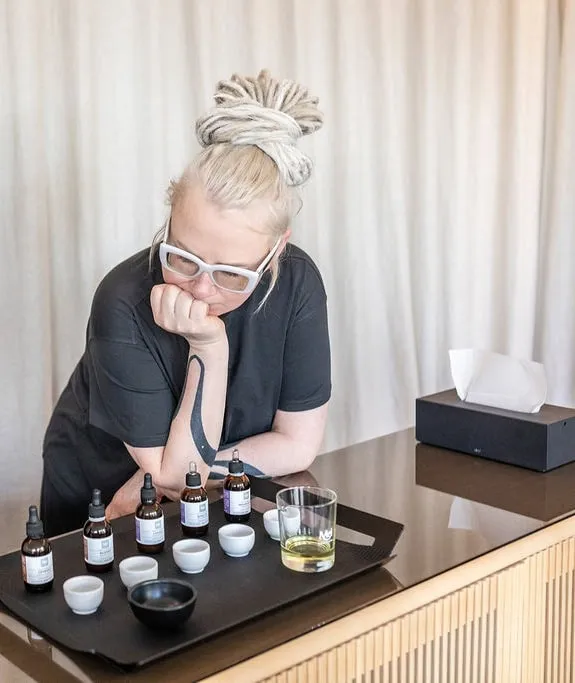 Woman at a table with bottles and jars of oil choosing a scent – “Sleeping Garden” ritual