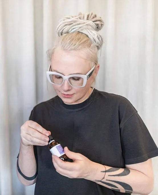 Woman with white glasses dripping oil from a bottle – “Sleeping Garden” wellness ritual