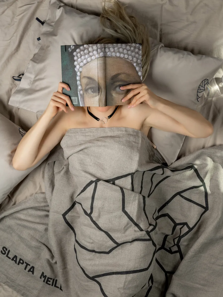 Moteris lovoje dengiasi veidą užrašine „Slapta meilė | Barbora Radvilaitė“