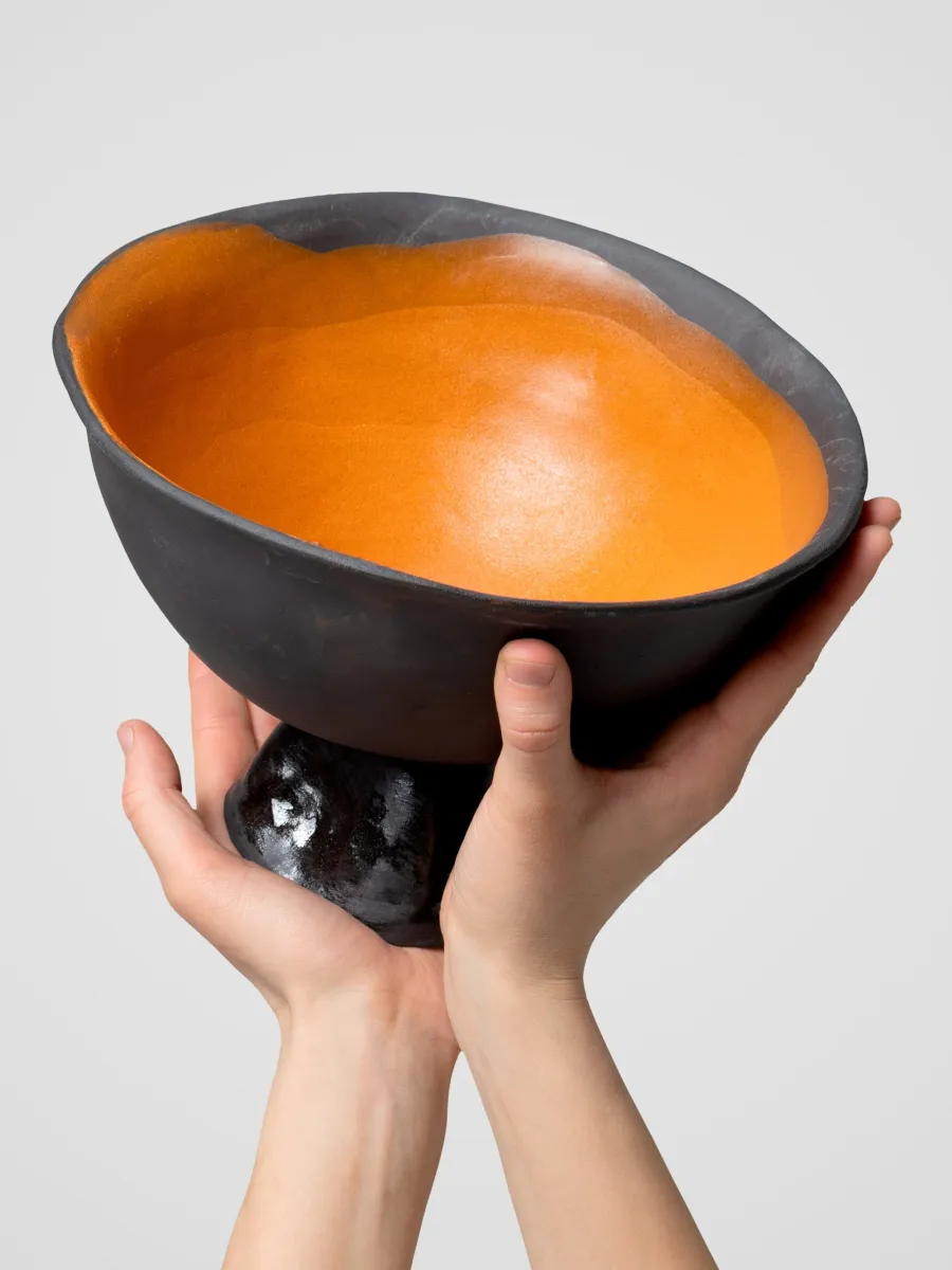 Hands lifting a black Kings' footed bowl with an orange interior