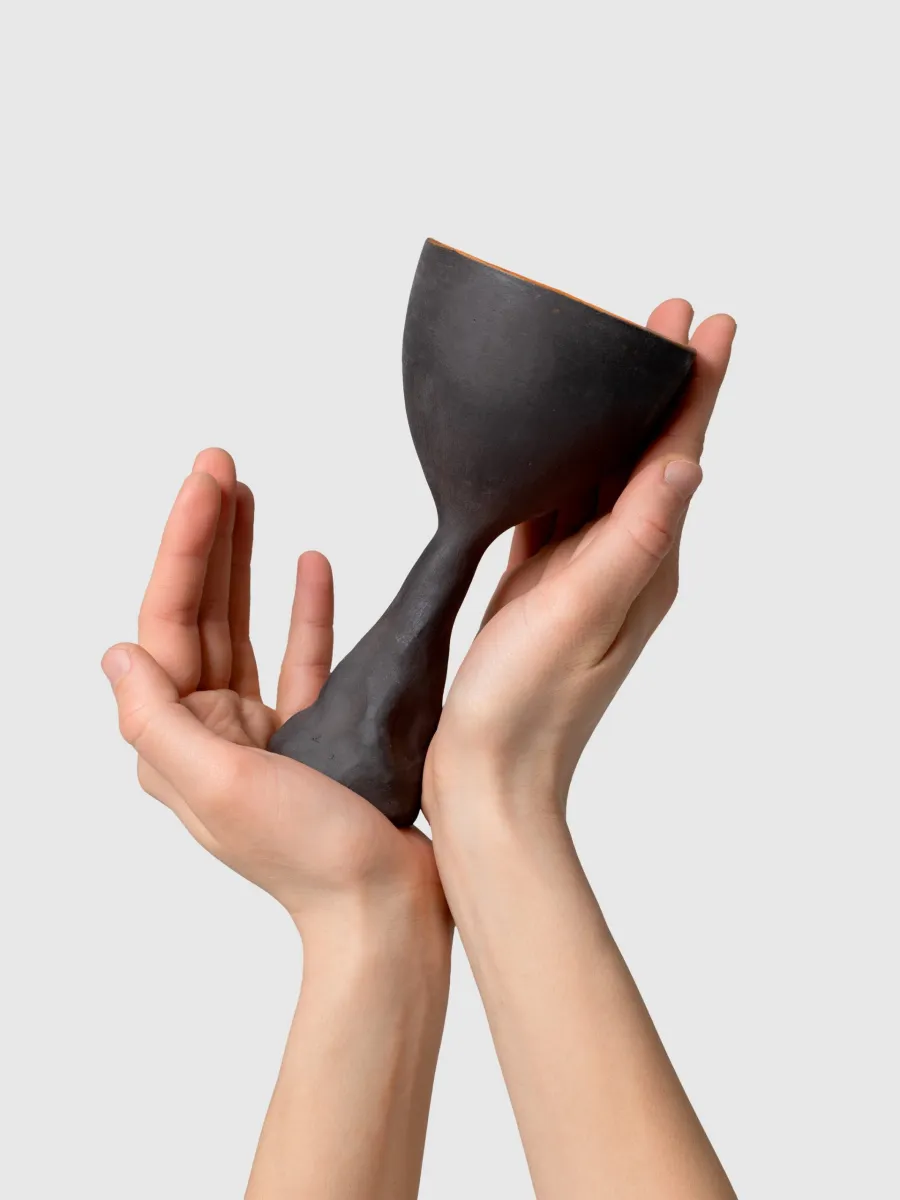 Two hands hold a black Kings' Goblet with a sculpted stem, angled view