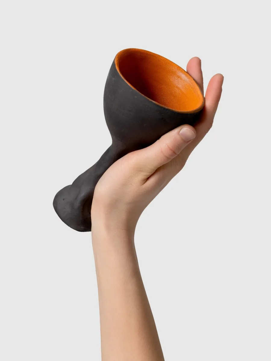 Hand holding a tilted black Kings' goblet, showing the orange glaze inside