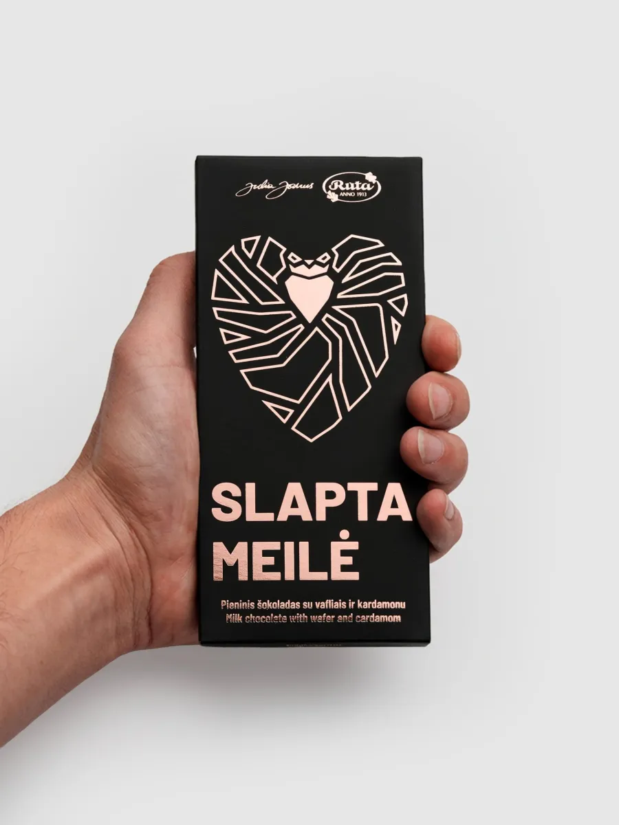 Black packaging of “Slapta meilė” milk chocolate with a pink heart, in a hand