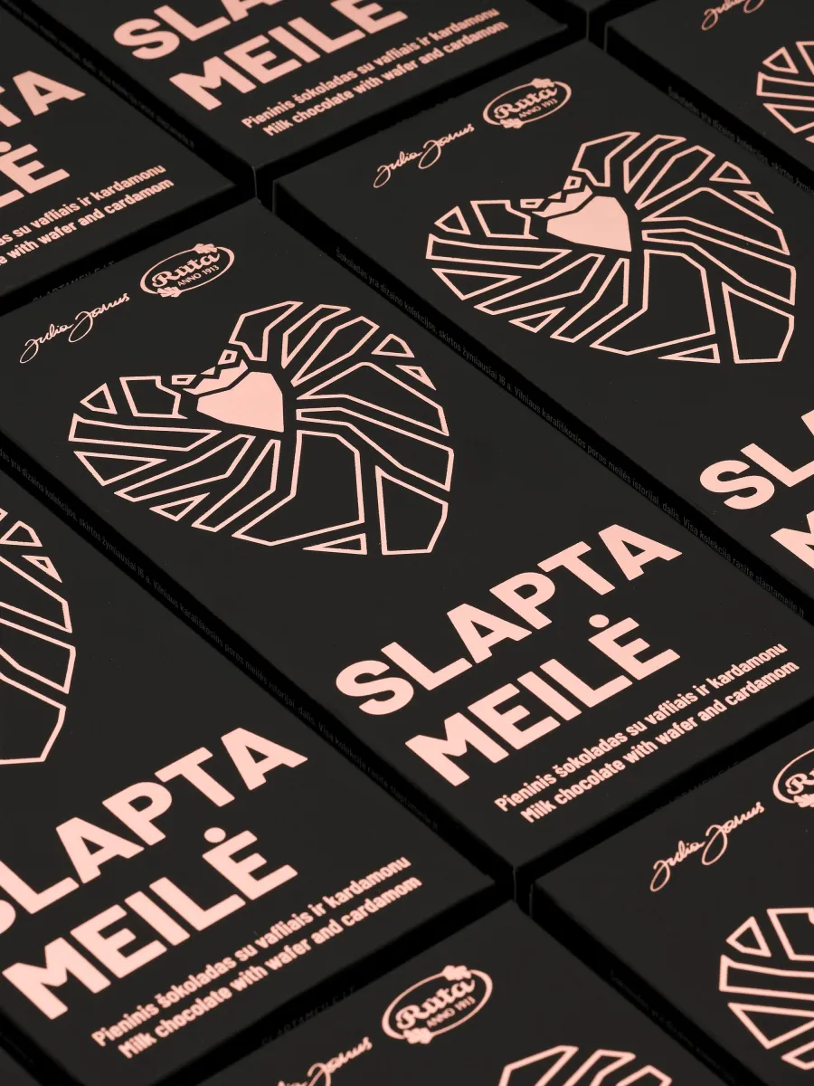 Many black “Slapta meilė” milk chocolate wrappers with a heart drawing, laid out in rows