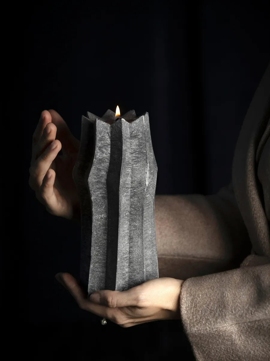 Burning anthracite candle “King Sigismund Augustus” in hands on a dark background