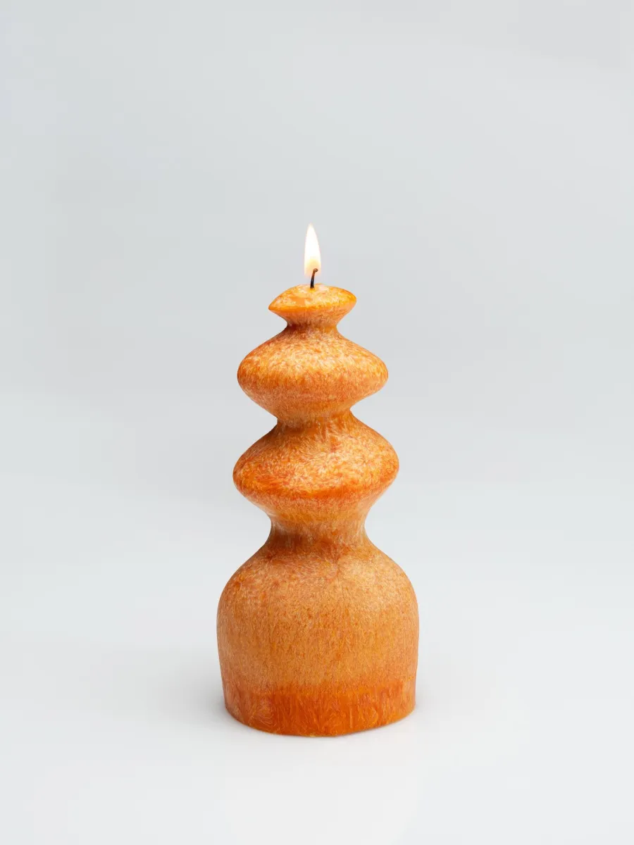 Orange wave-shaped candle “Queen Barbara” burning on a light background