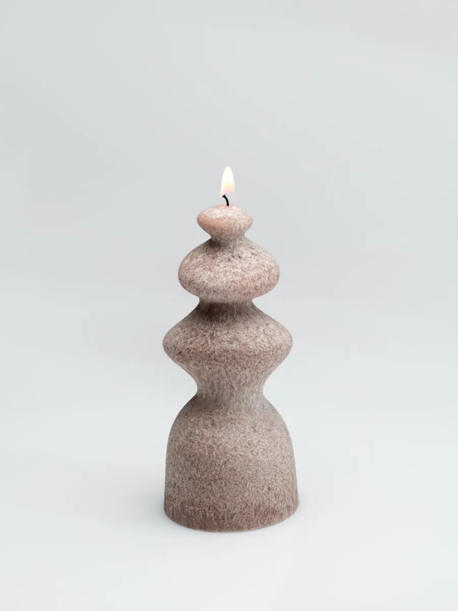 Powder-coloured wave-shaped “Queen Barbara” candle burning on a light background