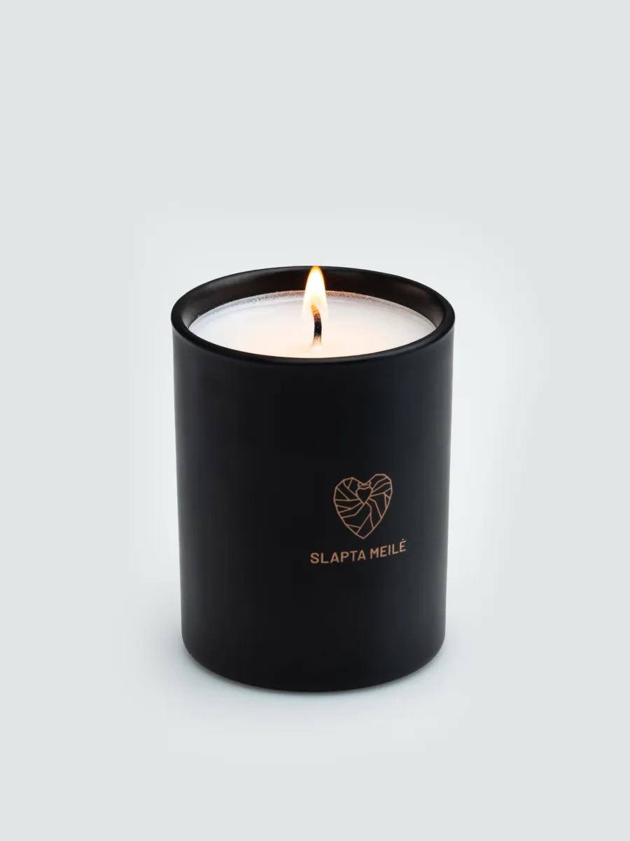 Lit “Slapta meilė” soy wax candle in a black jar with a copper-coloured heart logo