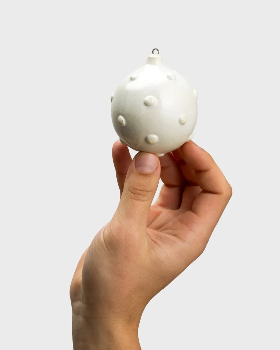 Hand holding a white collectible “Royal Pearl” Christmas ornament with a pearl relief