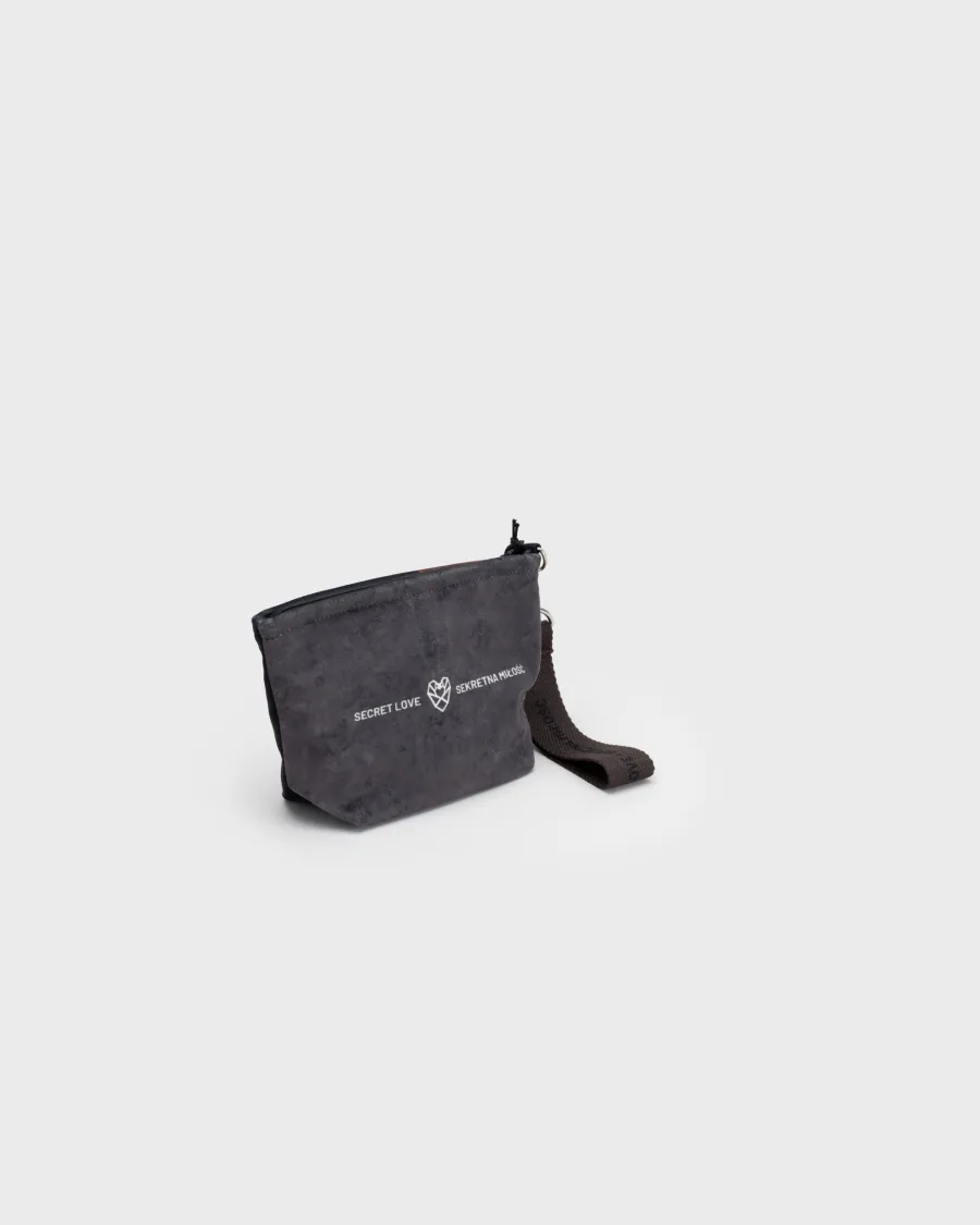 Back of the smallest dark grey “Augustus” cosmetic bag with a heart logo on a light background