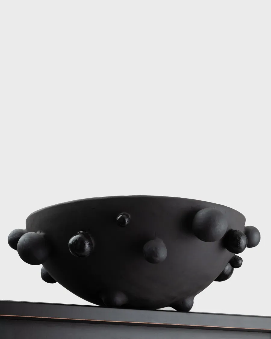 Side of the large matte black “The Queen's Pearl Bowl” with beads on the edge of a shelf