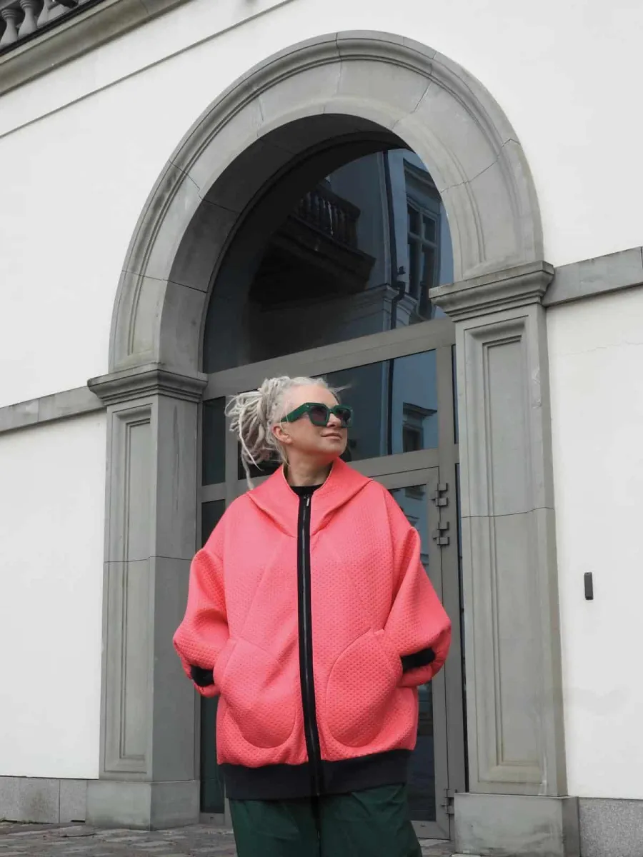 Woman in a coral “Rebel Queen” hoodie by an arched door, front
