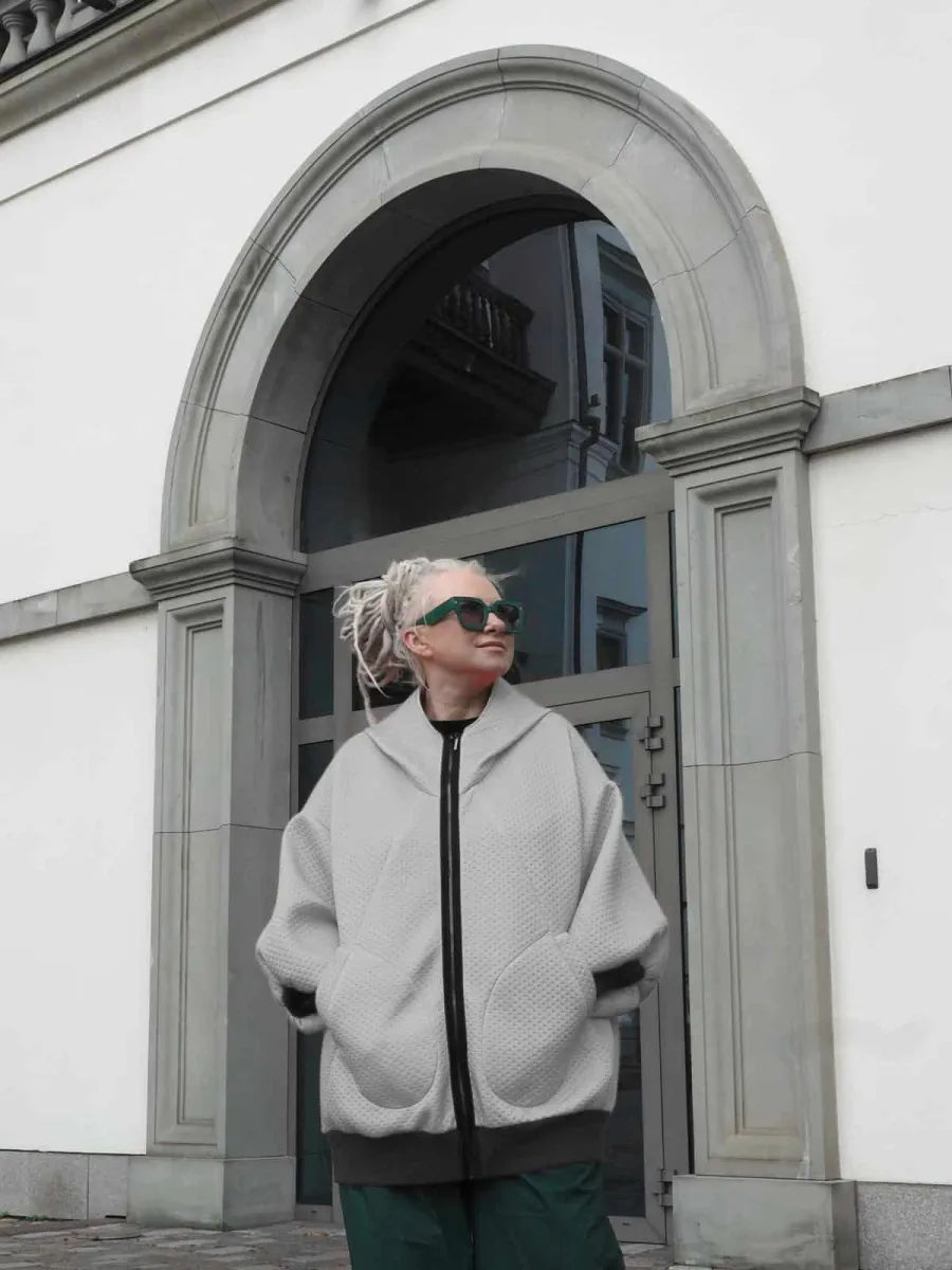 Woman in a grey “Rebel Queen” hoodie by an arched door, front view