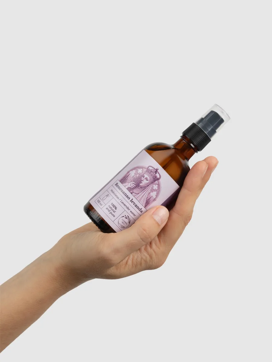 A brown glass spray bottle of “Renaissance Lavender” lavender hydrosol held diagonally in a hand