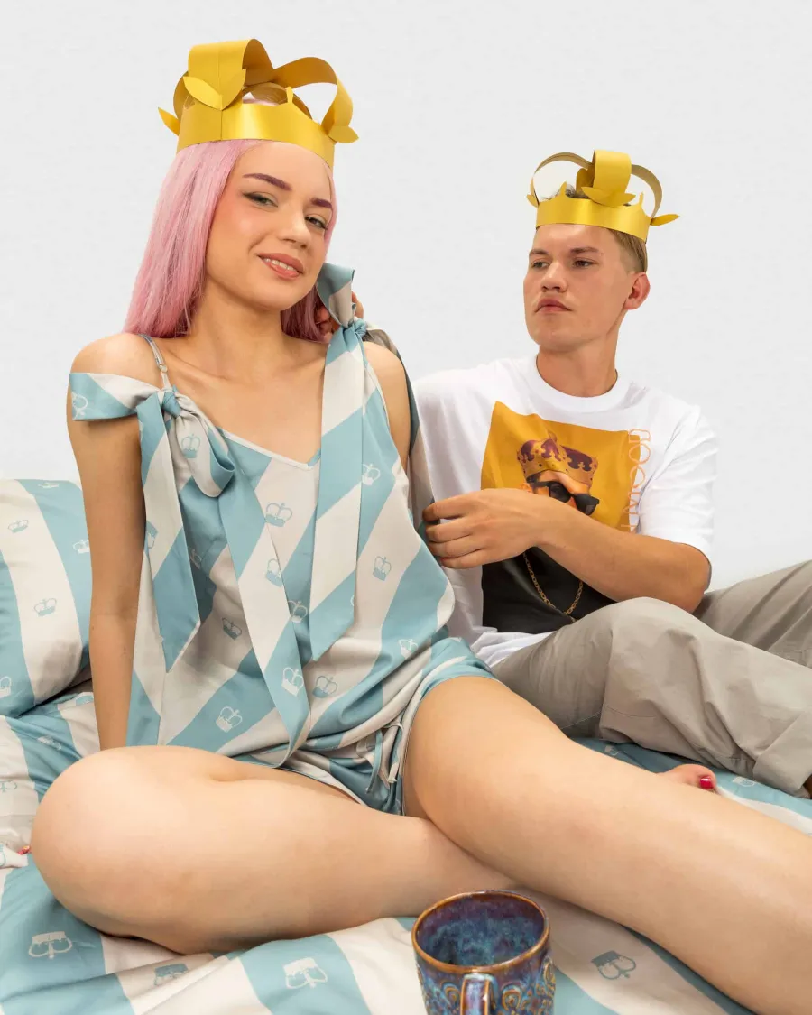 Girl and young man with golden paper crowns sitting on blue striped bedding