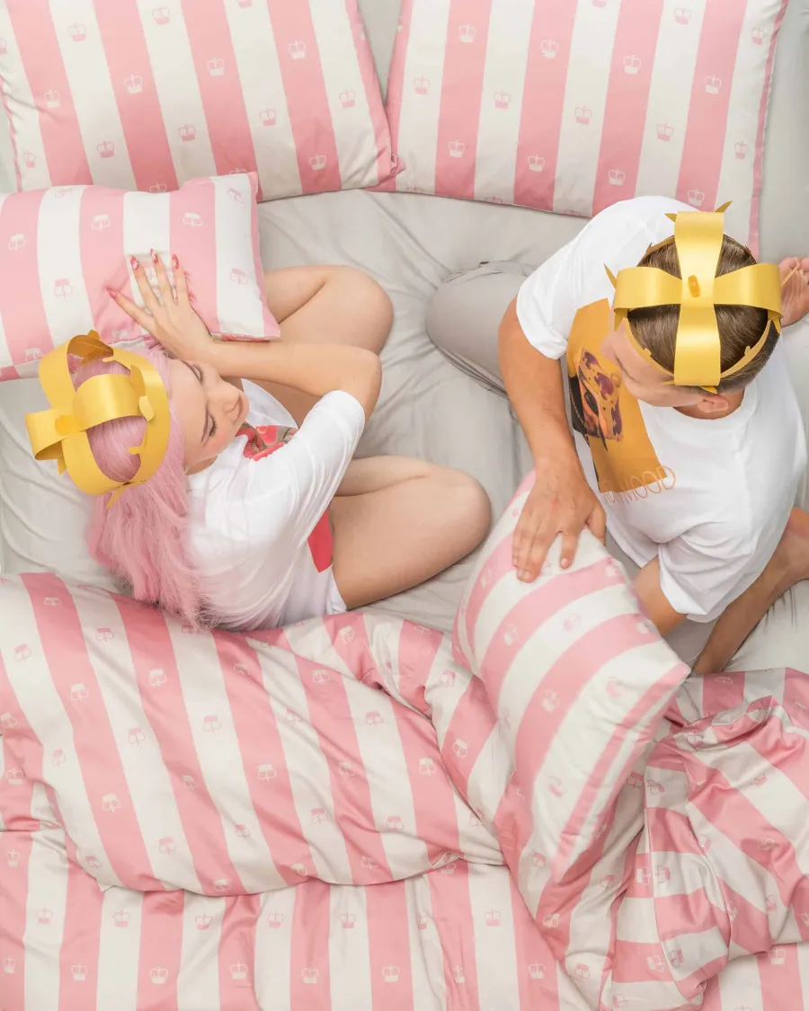 Couple with gold crowns lying in bed with pink and white striped bedding, view from above