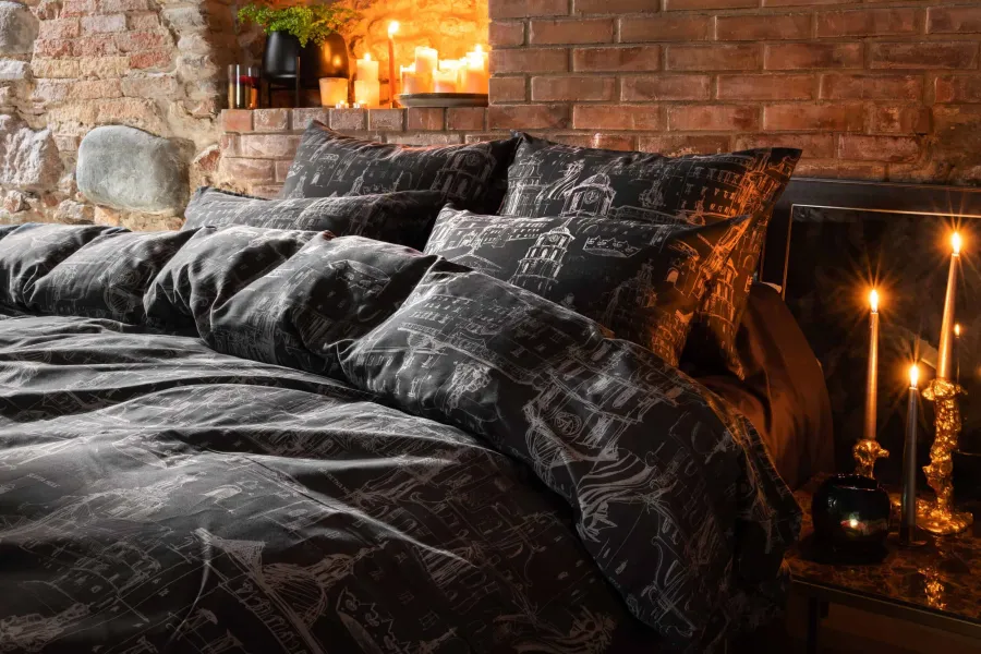 Bed with dark bedding with Vilnius drawings by a brick wall with burning candles