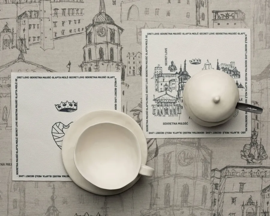 White teapot and cup on coasters with Vilnius drawings, top view