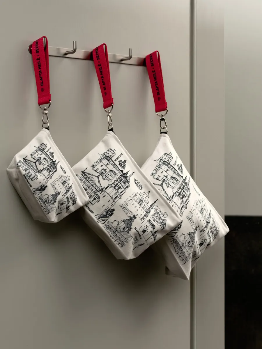 Three white cosmetic bags with Vilnius drawings and red ribbons hanging on hooks