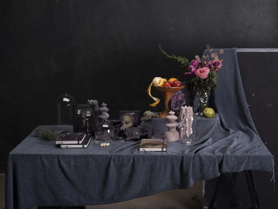 Long table with a dark tablecloth, candles, notebooks, flowers and fruit on a dark background