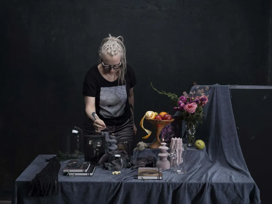 Blonde woman arranging a table with candles, notebooks and flowers in a dark room