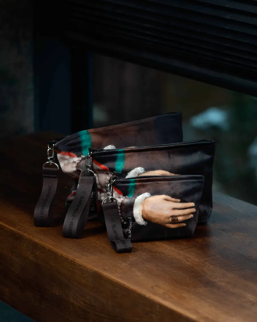 Dark leather cosmetic bags with a hand detail from a Renaissance portrait on a wooden surface