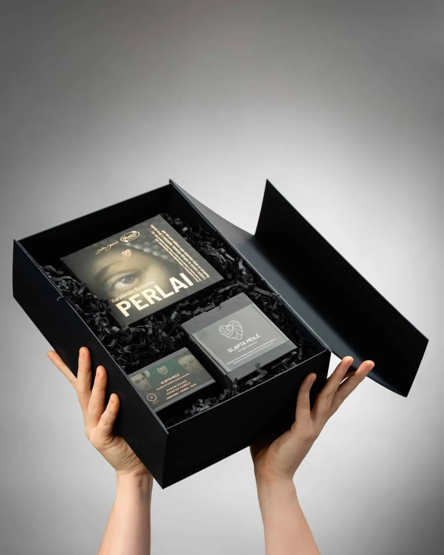 Hands holding a black gift box with “Queen Barbara's Pearls” sweets, a candle and ceramics