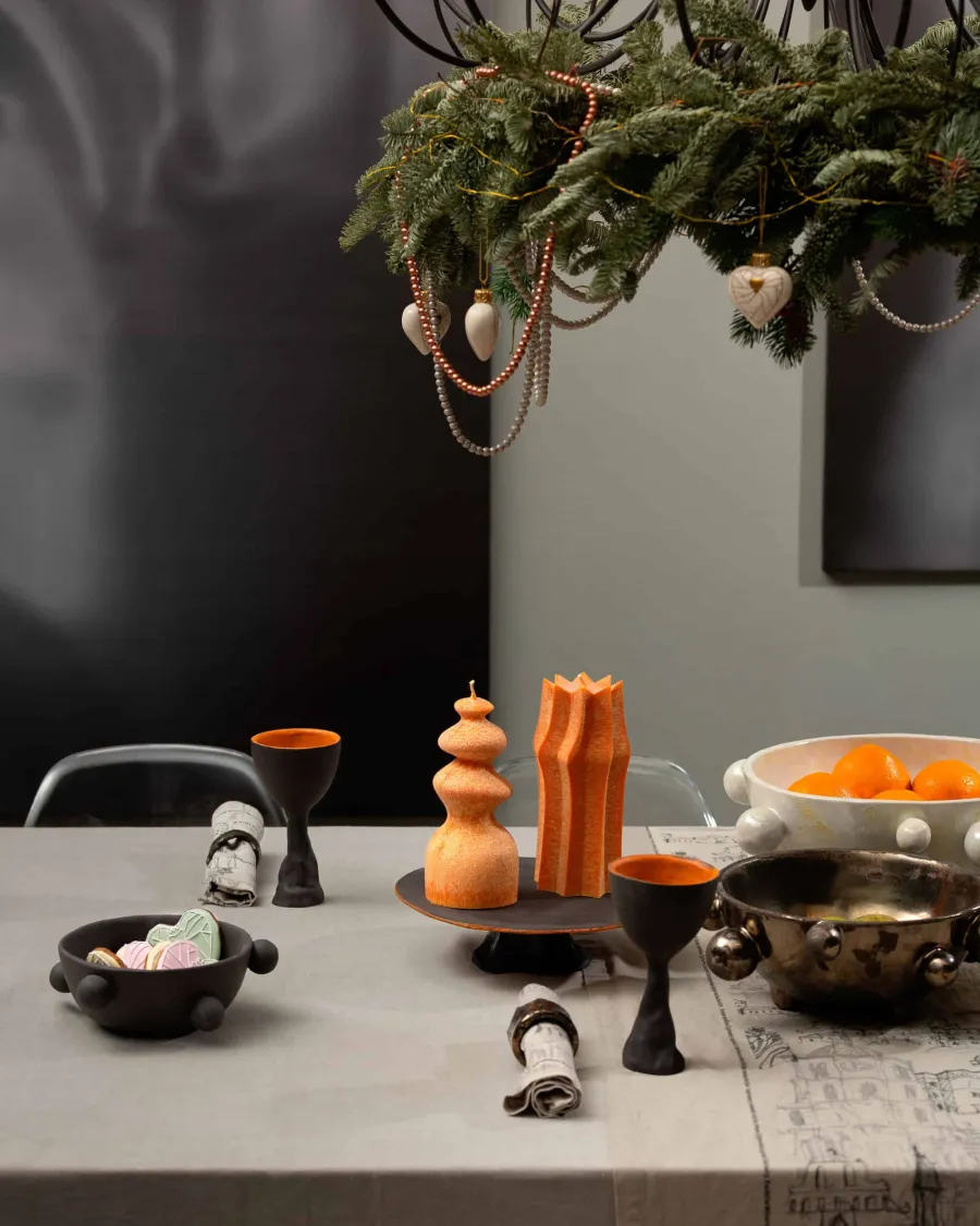 Grey table with orange candles, black ceramic dishes and tangerines under fir branches