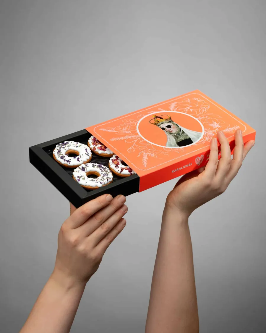 Raised hands hold an open orange box of pretzel-shaped sweets