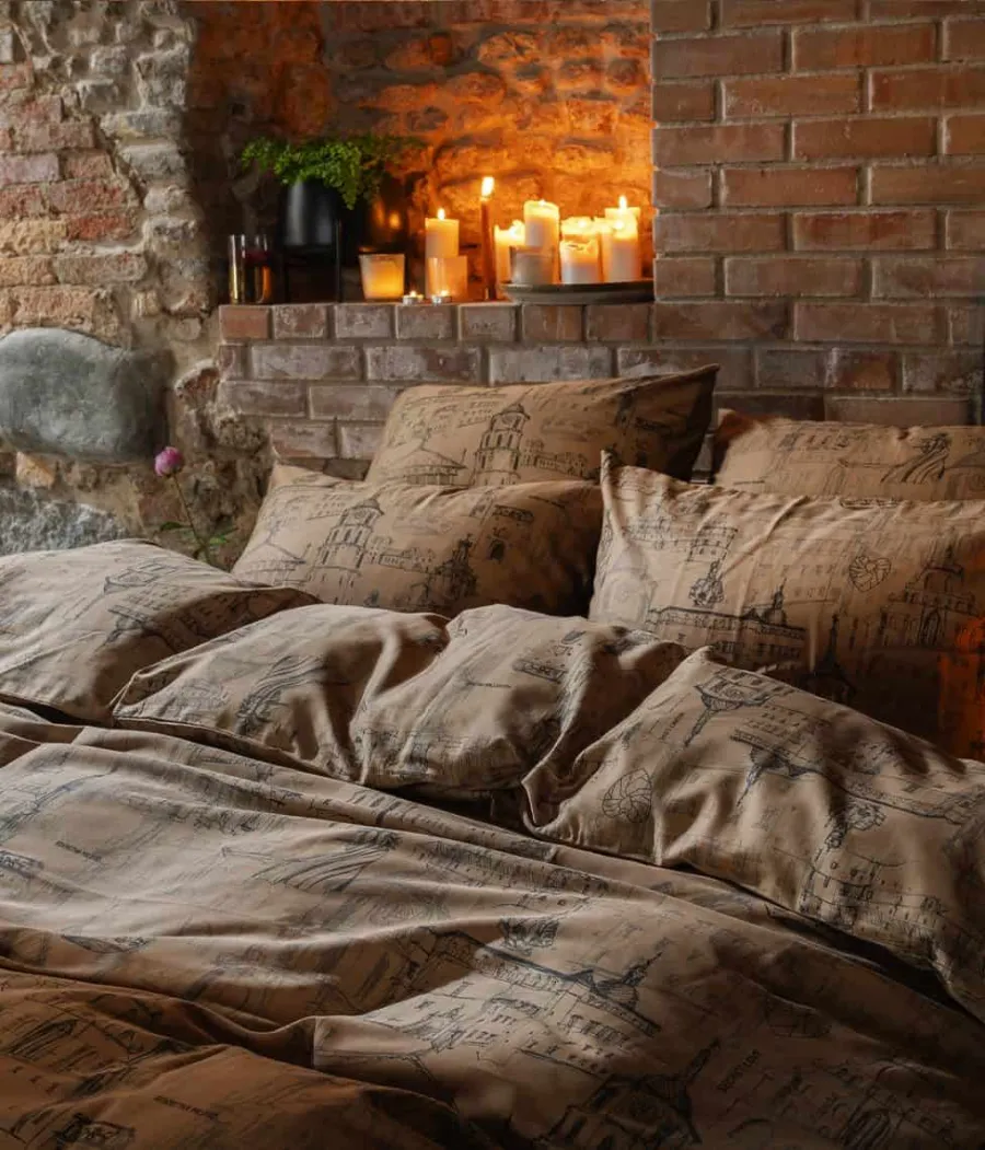 Cinamono spalvos satino patalynė „Karališko Vilniaus meilės istorija“ ant lovos prie plytų sienos ir žvakių